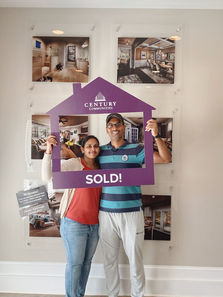 A man and woman holding a purple sign in a room with pictures on the wall.